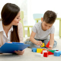 Young child psychologist evaluates little boy with clipboard as he plays