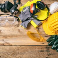 Construction safety. Protective hard hat, headphones, gloves and glasses on wooden background, copy space, top view