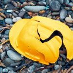 Cracked work helmet on the floor covered with pebble stones. Concept of work accident. Cracked work helmet on the floor covered with pebble stones. Concept of work accident.
