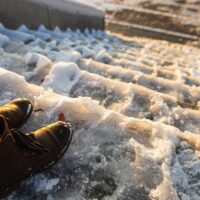 Danger of slipping. Female boots on rough slipper ice surface. A woman in brown leather shoes descends the slippery ice ladder