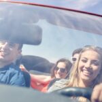 leisure, road trip, travel and people concept - happy friends driving in cabriolet car along country road