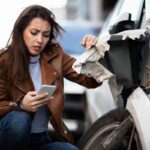 Displeased woman using cell phone and texting after a car accident in the city.