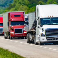 A solid line of eighteen-wheelers barrel down an interstate highway in Tennessee. Heat waves rising from the pavement give a nice shimmering effect to vehicles and trees behind the lead truck. A solid line of eighteen-wheelers barrel down an interstate highway in Tennessee. Heat waves rising from the pavement give a nice shimmering effect to vehicles and trees behind the lead truck.